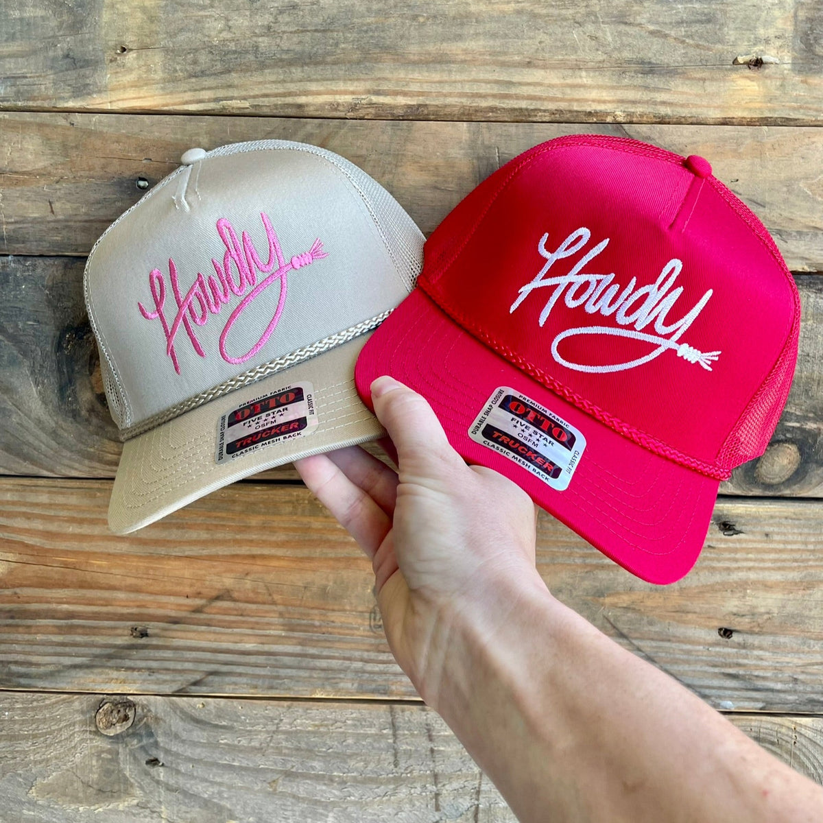 Two hats, one beige and one red, with 'Howdy' logo on a wooden surface.