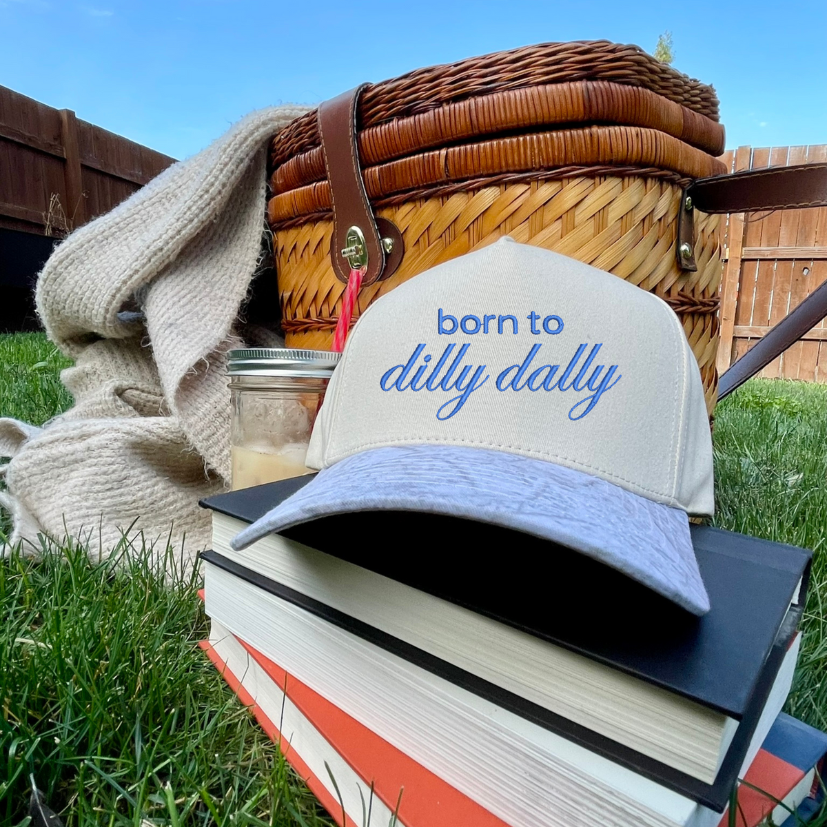 Cap with 'born to dilly dally' text on a stack of books outdoors