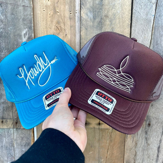 Two trucker hats, one blue and one brown, held against a wooden background.