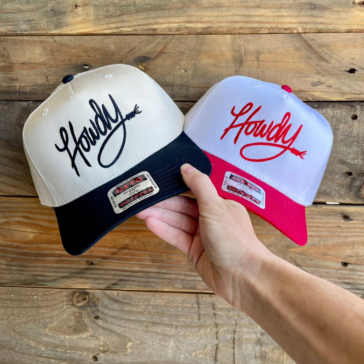 Two baseball caps with 'Howdy' embroidered text on a wooden surface