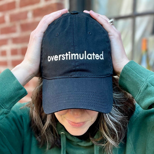 overstimulated embroidered in white on a black dad hat