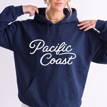 A woman wearing a navy blue hoodie with 'Pacific Coast' printed in white script across the chest, posed against a plain white background.